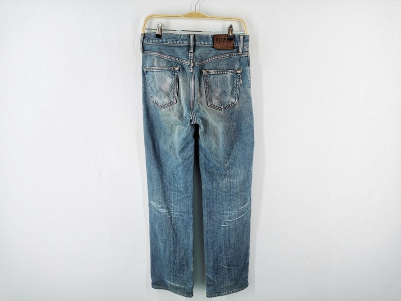 May include: Light blue denim jeans with a faded wash, hanging on a wooden hanger. The jeans have a classic five-pocket design, a leather patch with the brand name, and a straight leg fit.