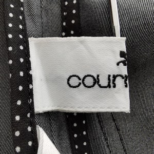 May include: Close-up of a white label with the word "count" in black script. The label is attached to a dark gray fabric with a subtle striped pattern. A black and white polka dot trim is visible.