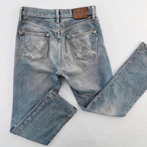 May include: Light blue denim jeans with a faded wash. The jeans have a classic five-pocket design, a straight leg, and a leather patch with the brand name "EDWIN" on the back. The jeans are laid flat on a white surface.