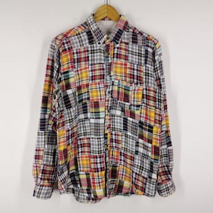 Pode incluir: Uma camisa de manga comprida com botões e um design de patchwork multicolorido. A peça é composta por vários painéis de tecido quadrados em tons de amarelo, vermelho, azul, preto e branco, dispostos num padrão de grelha com bolso.