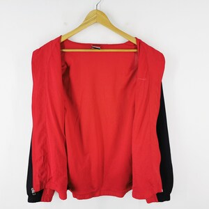 May include: A red and black zip-up jacket hanging on a wooden hanger. The jacket has a red interior and black sleeves. The zipper is closed at the bottom. The jacket is against a white background.
