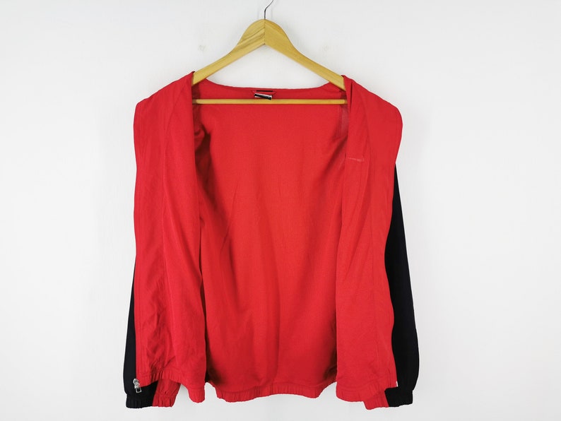 May include: A red and black zip-up jacket hanging on a wooden hanger. The jacket has a red interior and black sleeves. The zipper is closed at the bottom. The jacket is against a white background.