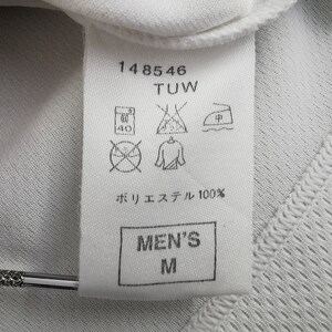 May include: Close-up of a white garment label with the text "148546 TUW". The label features care symbols and the text "ポリエステル 100%" and "MEN'S M". The garment has a textured, breathable fabric.