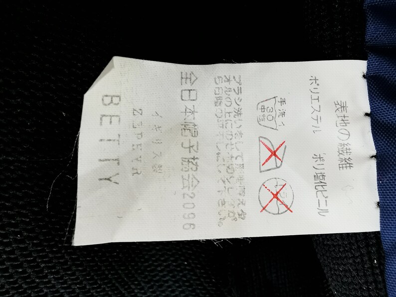 May include: A white tag with Japanese text and care symbols, including a hand wash symbol and a no-dry-clean symbol. The tag also includes the word "BETTY" and "ZEPEYR".