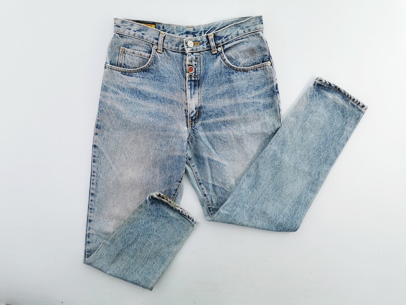 Op de afbeelding: Lichtblauwe denim jeans met een vervaagde wassing. De jeans heeft een knoop- en ritssluiting, een klassiek vijf-zakken ontwerp en een rechte pijp. De jeans ligt plat op een witte ondergrond.