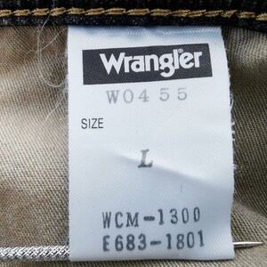 Peut inclure: Gros plan sur une &eacute;tiquette blanche avec le logo Wrangler et le texte "W04 55". L'&eacute;tiquette indique &eacute;galement la taille "L" et les codes "WCM-1300" et "E683-1801". L'&eacute;tiquette est fix&eacute;e &agrave; du tissu denim.