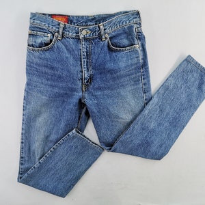 Puede incluir: Vaqueros de mezclilla azul claro con un dise&ntilde;o cl&aacute;sico de cinco bolsillos. Los vaqueros tienen cierre de bot&oacute;n y cremallera, trabillas para el cintur&oacute;n y un lavado descolorido. La marca "EDWIN" es visible en una etiqueta roja.