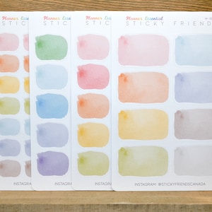 May include: Four sheets of colorful watercolor planner stickers with rounded rectangular shapes. The stickers are in shades of pink, blue, yellow, and green. The sheets are labeled "Planner Esse STICKY" and "Planner Essential STICKY FRIENDS".