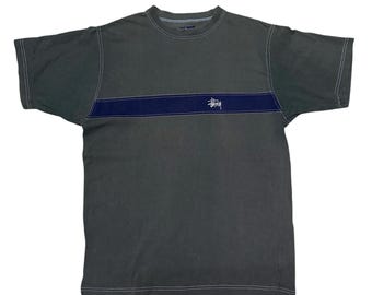 May include: A dark green short-sleeved t-shirt with a navy blue stripe across the chest and the word "Stüssy" in white lettering.