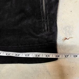 May include: Close-up of black corduroy fabric with a zipper. A measuring tape shows the fabric is approximately 40 cm wide. The corduroy has a ribbed texture.