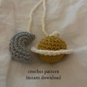 May include: Crochet pattern for a moon and planet mobile, with a gray crescent moon and a yellow planet with a white ring. The pattern is available for instant download.