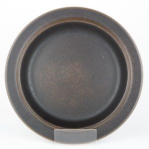 Könnte beinhalten: Ein runder, dunkelbrauner Keramikteller mit leicht erhöhtem Rand. Der Teller hat eine matte Oberfläche und ein schlichtes Design. Der Teller eignet sich zum Servieren von Speisen. Durchmesser ca. 25 cm.