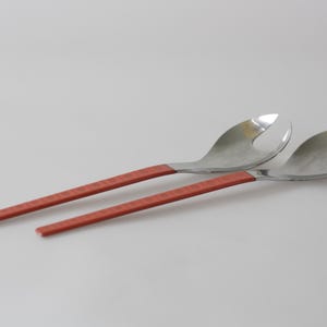 Peut inclure: Une paire de couverts à salade avec des têtes en acier inoxydable et des manches texturés, orange rougeâtre. L'un a une tête fendue, l'autre une tête en forme de cuillère. Ustensiles pour servir les salades.