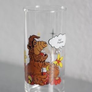 Könnte beinhalten: Ein klares Trinkglas mit einer farbigen Grafik der Figur ALF, die ein rotes Getränk mit einem Strohhalm hält. Eine weiße Sprechblase über der Figur enthält den Text "No Problem". Das Design zeigt zudem gelbe und rote Blumen.