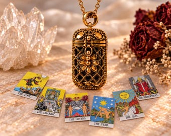 May include: A gold-toned metal locket pendant with an intricate lattice design and a central flower motif, suspended on a chain. Below the pendant are six tarot cards labeled The Fool, The Chariot, The Lovers, The Star, The Sun, and The Hierophant.