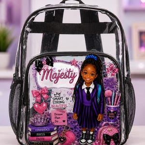 May include: A clear plastic backpack featuring a graphic print of a character in a purple striped uniform. The design includes the text Majesty, Smart Strong Beautiful, and Dream Plan Do, along with images of books, a crown, and a small pink backpack.