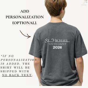 May include: A gray t-shirt with the text "St. Michael Youth Group 2026" printed on the back in white. The shirt also has text that says "Add Personalization (Optional)" and "If no personalization is added, the shirt will be shipped with no back text."