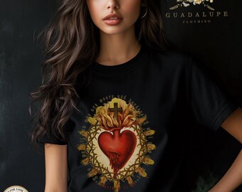 May include: A black t-shirt featuring a graphic of a red Sacred Heart with a cross and flames, encircled by a crown of thorns. The design includes text surrounding the heart. The upper right corner displays the text GUADALUPE CLOTHING.