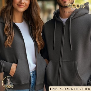 May include: Two people wearing dark heather gray zip-up hoodies. The hoodies have front pockets and drawstrings on the hood. The text "UNISEX-DARK HEATHER" is at the bottom of the image.