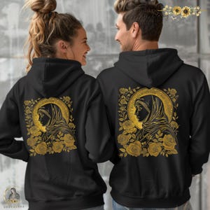 May include: Black hooded sweatshirts featuring a gold illustration of a religious figure surrounded by roses. The design is on the back of the sweatshirts. The sweatshirts are worn by two people.