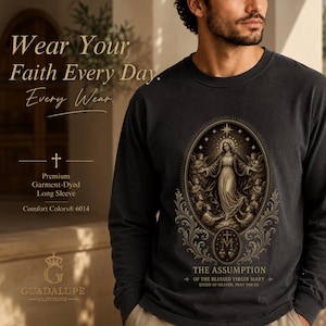 Peut inclure: Un t-shirt à manches longues gris anthracite avec un graphique détaillé de l'Assomption de la Sainte Vierge Marie entourée d'anges dans un cadre ovale. Le texte indique : Wear Your Faith Every Day. Every Wear. Premium Garment-Dyed Long Sleeve.