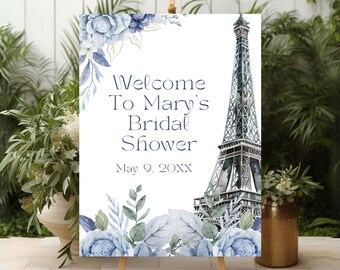 Könnte beinhalten: Ein weißes Willkommens-Schild mit blauen und goldenen floralen Akzenten und einer Aquarell-Illustration des Eiffelturms. Das Schild lautet "Willkommen zum Bridal Shower von Mary am 9. Mai 20XX".