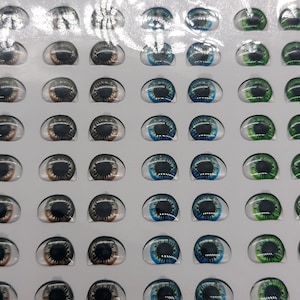 May include: A sheet of plastic-covered paper with 48 pairs of doll eyes. The eyes are arranged in rows of 4, with each row featuring a different colour: brown, black, blue, and green.