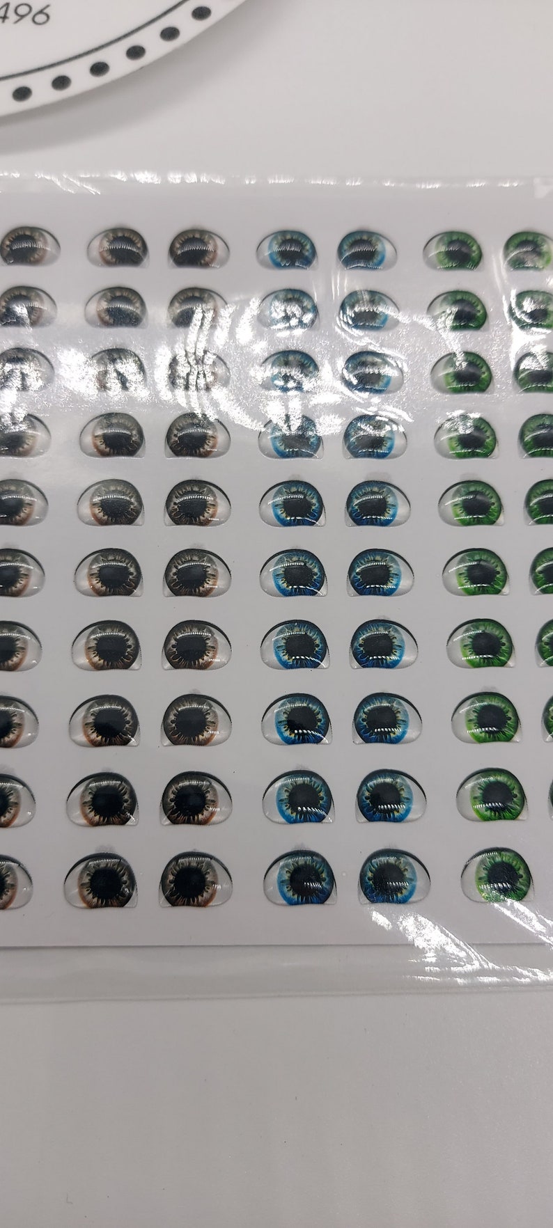 May include: A sheet of plastic-covered paper with 48 pairs of doll eyes. The eyes are arranged in rows of 4, with each row featuring a different colour: brown, black, blue, and green.
