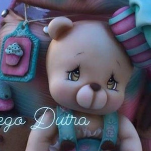 May include: A white porcelain bear figurine with brown eyes and a brown nose. The bear is wearing a blue and white dress with a floral pattern. The bear is holding a cupcake in its right paw. The bear is surrounded by cupcakes and other decorations.