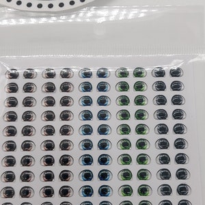 May include: A sheet of 55 pairs of doll eyes, with a variety of colours, including brown, blue, green, and grey. The eyes are 5 mm by 6.5 mm in size. The sheet is labelled "Humanizado 02" and "Niwia Arts PP".