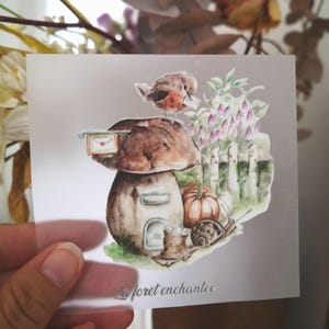 Peut inclure: Une illustration aquarelle d'une maison champignon avec un oiseau rouge perché sur le dessus. Le champignon a une petite porte et une fenêtre. Il y a une citrouille et un escargot devant la maison. Le texte "La forêt enchantée" est écrit sous l'image.