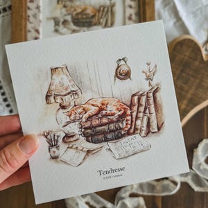 Peut inclure: Illustration à l'aquarelle d'un chat roux dormant sur des livres, à côté d'une lampe. L'image comprend un vase de fleurs, un livre ouvert et un journal. Le mot "Tendresse" est écrit en bas de l'œuvre.