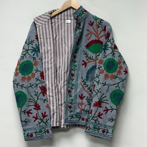 May include: A light grey jacket featuring vibrant floral embroidery in shades of green, red, and orange. The garment has a mandarin collar, long sleeves, and a brown and white vertical striped lining visible on the interior front panel.