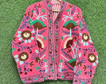 Op de afbeelding: Een felroze jas met lange mouwen, een hoge kraag en een open voorzijde. Het kledingstuk is over het gehele oppervlak versierd met ingewikkeld bloemen- en botanisch borduurwerk in tinten bruin, lichtblauw, donkerblauw en groen.