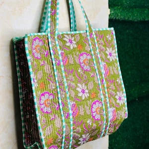 May include: A green quilted tote bag with a floral print and white and green striped trim. The bag has two handles.