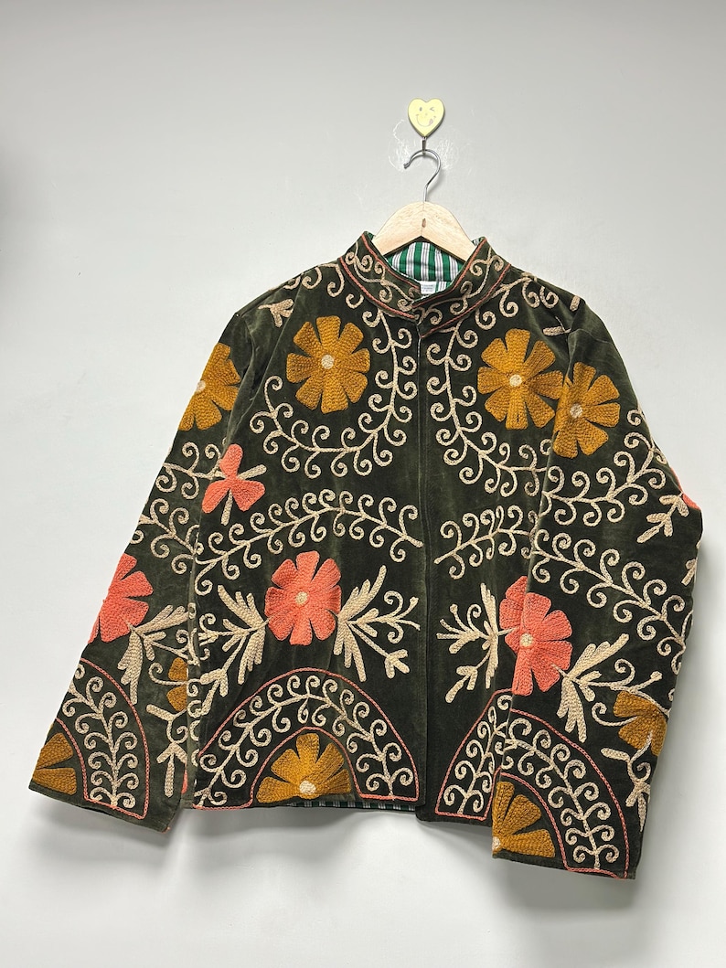 May include: Olive green jacket with floral embroidery in orange and yellow. The jacket features a mandarin collar and is adorned with intricate embroidered patterns. The design includes a mix of floral and scroll motifs, creating a vintage aesthetic.