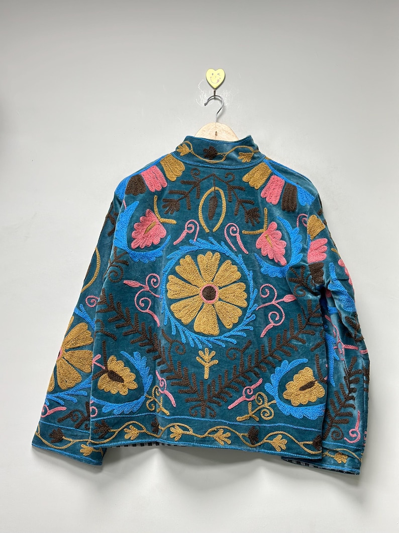 May include: A teal velvet jacket featuring intricate, multi-colored floral and leaf embroidery. The design includes large golden-yellow circular flower motifs, pink petals, and dark brown foliage patterns across the back and sleeves.