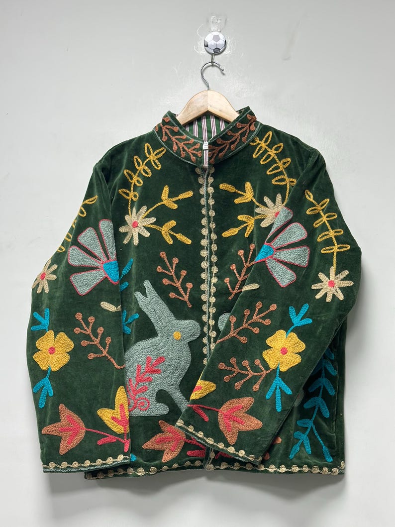 May include: A dark green velvet jacket featuring a front zipper closure and a high collar. The jacket is decorated with colorful embroidered motifs including a light green rabbit, yellow flowers, blue fan-shaped petals, and brown leaves.