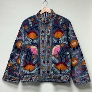 May include: A blue jacket featuring a high collar and long sleeves, decorated with intricate floral embroidery in shades of orange, pink, and dark red. The garment displays a symmetrical pattern of stylized flowers and vines across the front.
