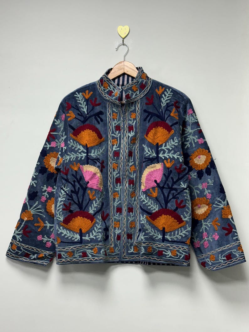 May include: A blue jacket featuring a high collar and long sleeves, decorated with intricate floral embroidery in shades of orange, pink, and dark red. The garment displays a symmetrical pattern of stylized flowers and vines across the front.