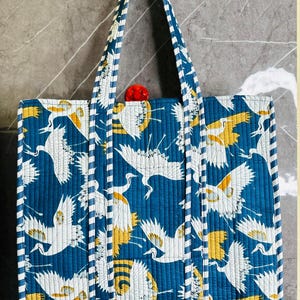 May include: A blue tote bag with white and yellow crane print. The bag has white and blue striped straps.