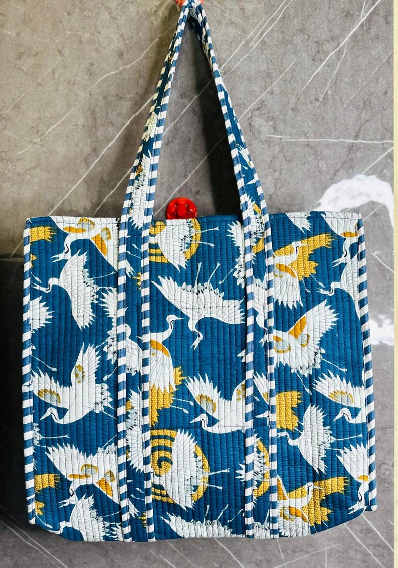 May include: A blue tote bag with white and yellow crane print. The bag has white and blue striped straps.