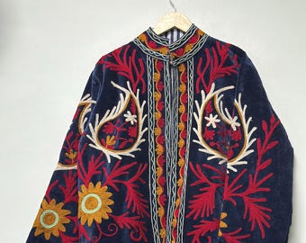 Puede incluir: Una chaqueta de terciopelo azul marino con intrincados bordados en rojo, amarillo y blanco. El diseño incluye motivos florales, formas de cachemira y bordes geométricos a lo largo del cuello, la abertura frontal y los puños. Cuello alto.