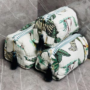May include: Three white quilted zippered pouches with a green and black jungle print. The pouches have black tassels and gold zipper pulls.