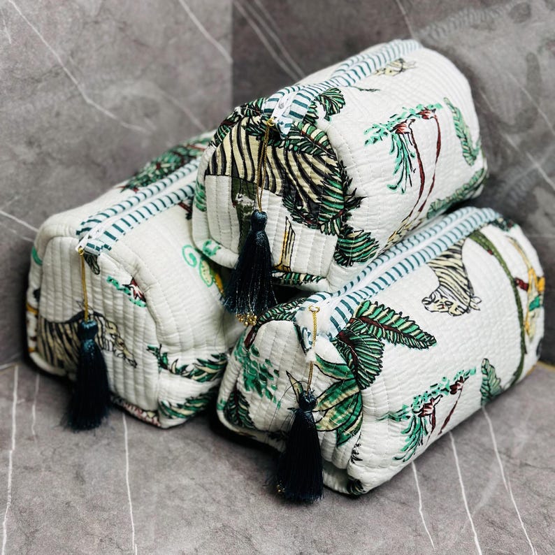 May include: Three white quilted zippered pouches with a green and black jungle print. The pouches have black tassels and gold zipper pulls.