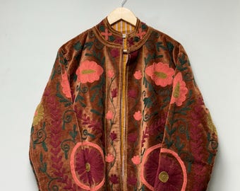 May include: A brown velvet jacket with intricate floral embroidery in shades of red, pink, and green. The jacket features a high collar, a full-length zipper, and is hanging on a wooden hanger.