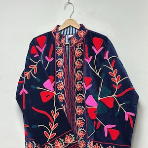 Op de afbeelding: Een marineblauw fluwelen jasje met levendig bloemenborduursel in tinten rood, roze en donkergroen. Het kledingstuk heeft een opstaande kraag, lange mouwen en een opening aan de voorzijde met verticale geborduurde patronen langs de sluiting.