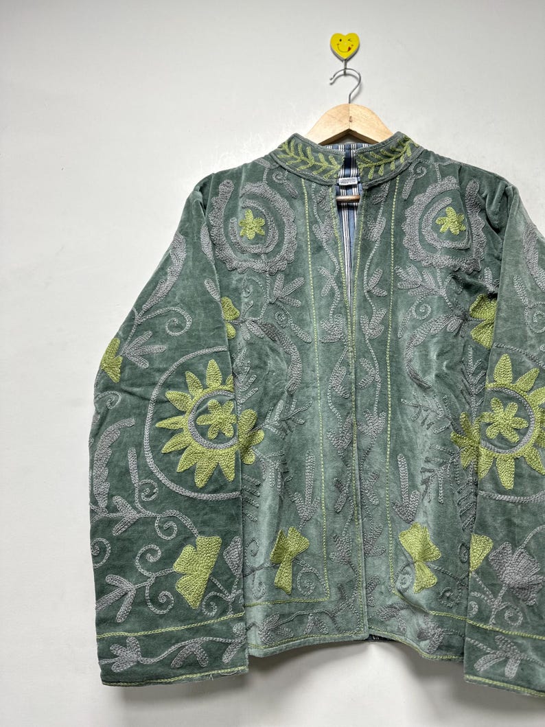 May include: A green velvet jacket with intricate floral embroidery in shades of gray and chartreuse. The jacket features a high collar and a full-length zipper. The design includes stylized flowers and leaf patterns.