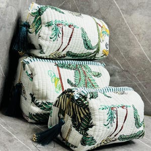 May include: Three white quilted zippered pouches with a tropical print featuring palm trees, leaves, and animals. The pouches have green and blue trim and tassels.