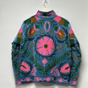 May include: A blue jacket with a high collar and intricate floral embroidery in pink, green, and brown. The jacket is hanging on a wooden hanger. The floral design is centered on the back.